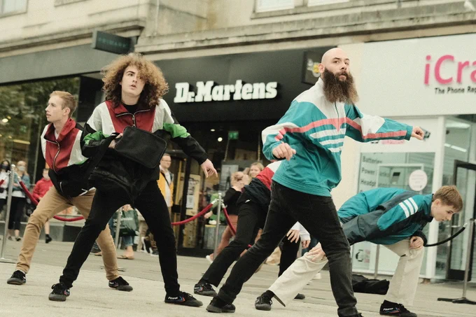 A colour photo of 4 male dancers holding black bags 