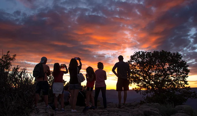 Several people are silhouetted by a vibrant sunset, with yellow and tangerine tones. NPS/M.Quinn