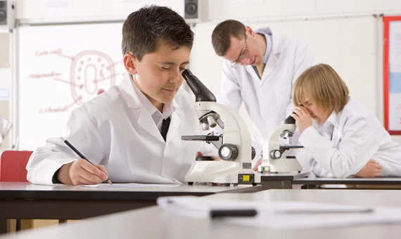 boy wearing a labcoat looking through a microscope in a classroom