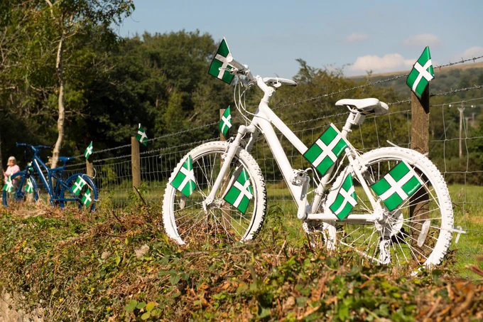 A bike leaning against a fence and covered in Devon flags.