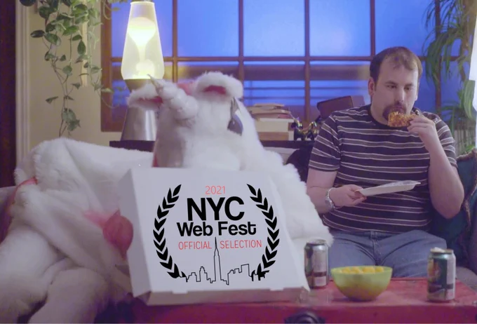 A screenshot from Unicorn Included episode four, of Unicorn and Jonathan eating pizza on their couch. An NYC Webfest logo is pasted on top of the pizza box.