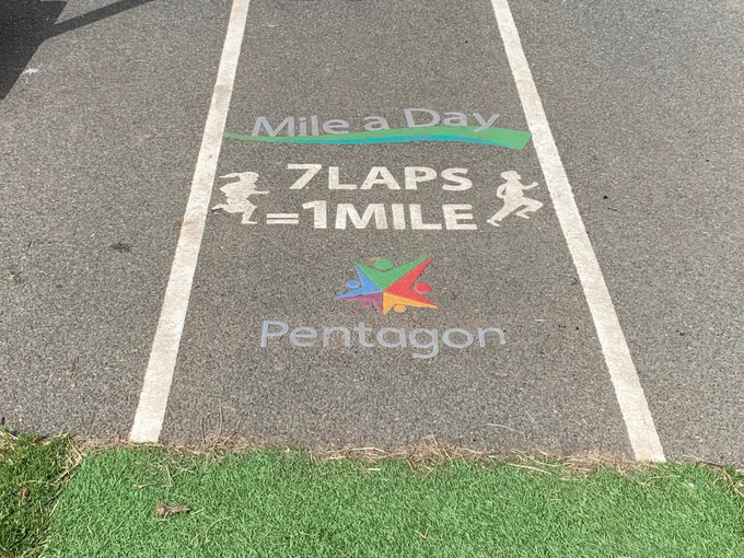 a zoomed in picture of our daily mile track details, the distance is noted at 7 laps equalling 1 mile, the pentagon logo is vibrant against the tarmac and the track is labelled as 'mile a day'