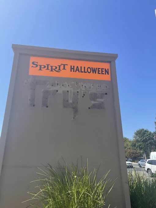 The disgraced remains of a Fry’s Electronics sign papered over with a Spirit Halloween banner.