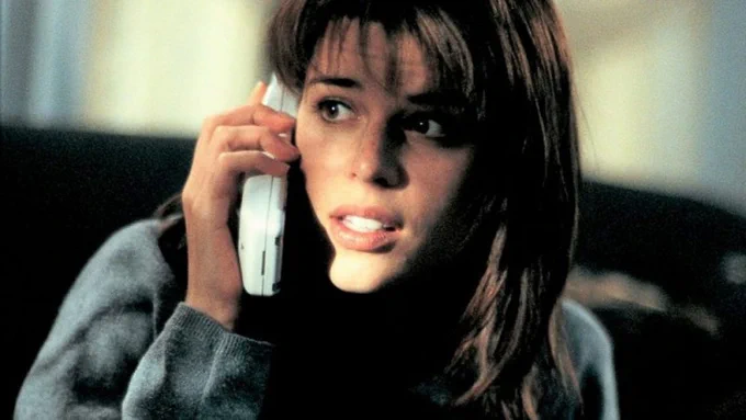 Neve in an iconic scene from Scream of her on the phone. She's holding the white phone to her ear and is looking worried.
