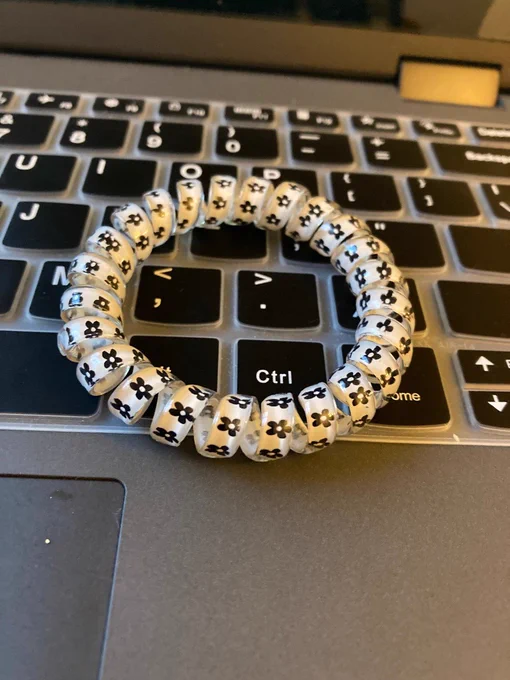 a white phone cord bracelet with black flowers sitting on a dark gray laptop keyboard.