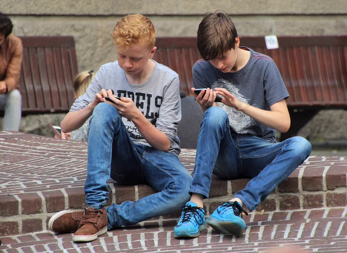 Two teenagers stare intensely at their smartphones while touching the phones' screens.