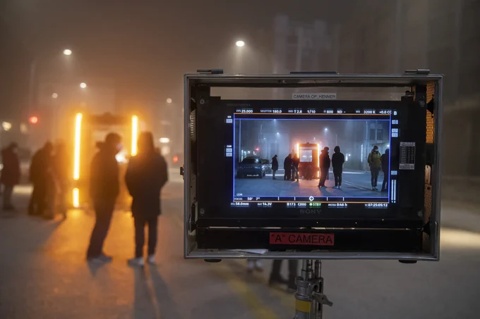 Olli is shown in the foreground on a camera view screen and in the background with film crew members preparing the vehicle for filming.
