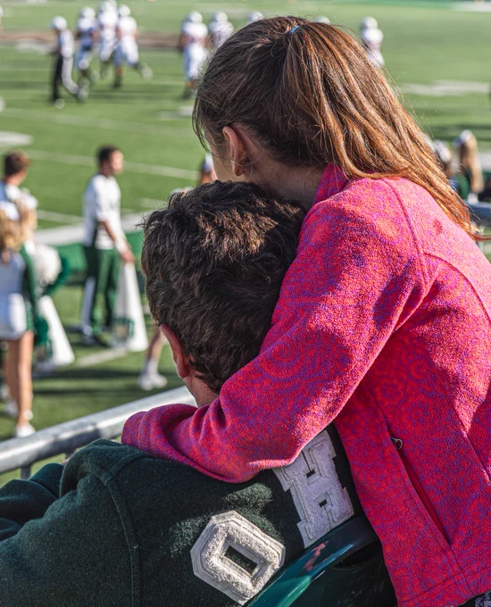 Young girl hugs a family member in an Ohio University Alumni Marching 110 jacket.