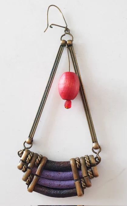 A triangular shaped earring with a purple and gold band across the bottom, and a large red bead hanging inside the top of the triangle. It has a lockable hook.