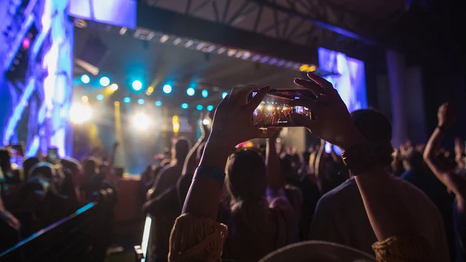 People enjoying a performance at the mainstage of Calgary folk fest. One person with arms raised holding a phone and recording the performance. 