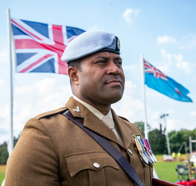 Fijian officer in the British Army with Union Flag and Fijian flag flying behind him.