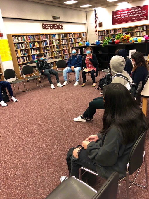 Students sitting in a circle and Librarian Mrs. Barbuzza welcoming them to the library.