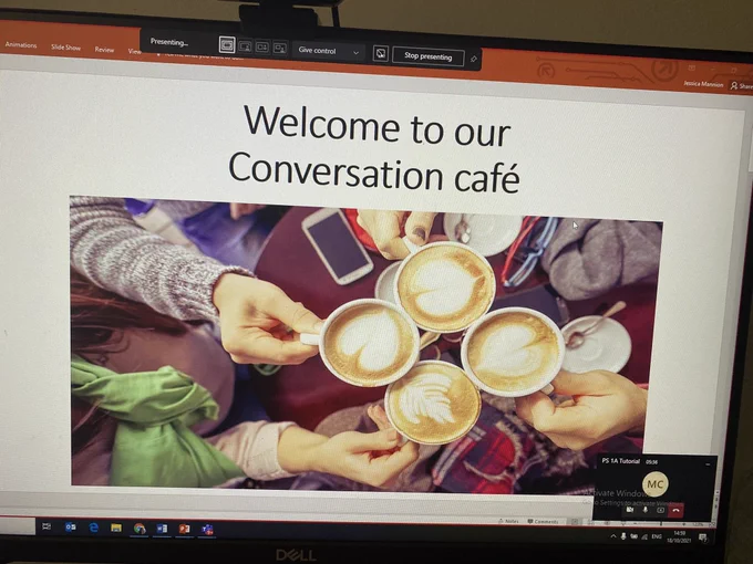 Photo of power point screen saying welcome to our conversation cafe and a photo of people with mugs of coffee sat together