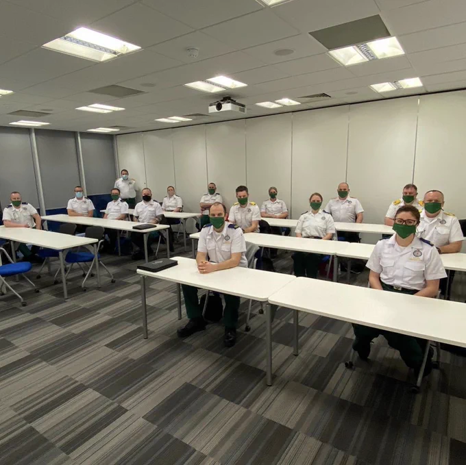 A classroom of paramedics, each wearing masks and smiling at the camera 