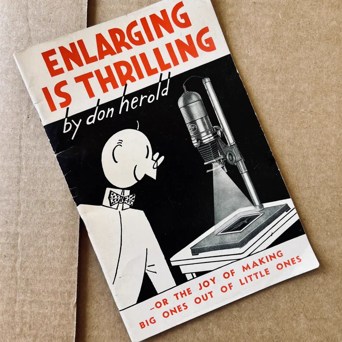 A booklet by Don Herold with the title “Enlarging Is Thrilling” and the subtitle “Or The Joy Of Making Big Ones Out Of Little Ones.” The cover image is of a cartoon character next to an enlarger used to produce photographic prints from film negatives.