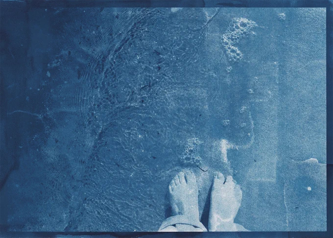 muted blue cyanotype image of feet being washed by waves on the shore