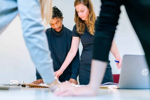 Team standing and discussing a project, viewed from low angle as they lean arms on a table and sort through papers