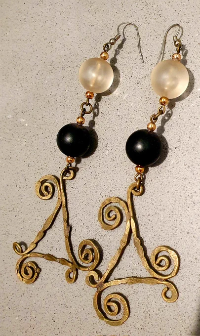A pair of gold curlicue earrings, each has a clear white bead above a solid black bead above the curly bit at the bottom.