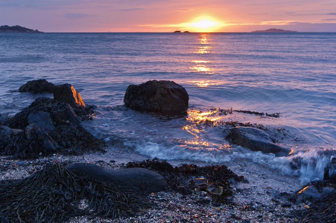 Rocks and sea with the sun rising over the horizon