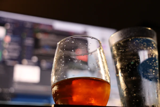 an amber beverage with ice in a glass, next to a pint of water, in front of a blurry computer monitor