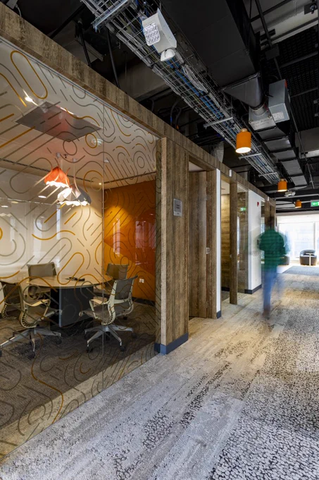 A person walks down a hallway past a meeting room, which has a glass wall separating the hallway from the meeting room. 