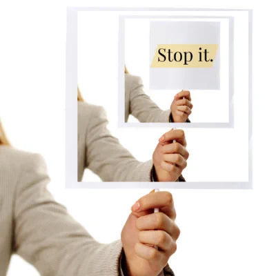 A person looms off frame holding a sign against a white background. The sign has the exact same image on it creating this rabbit hole-like effect. The final sign has the words ‘Stop it.’ written on it. The phrase is highlighted – as if someone has used a yellow highlighter on it.