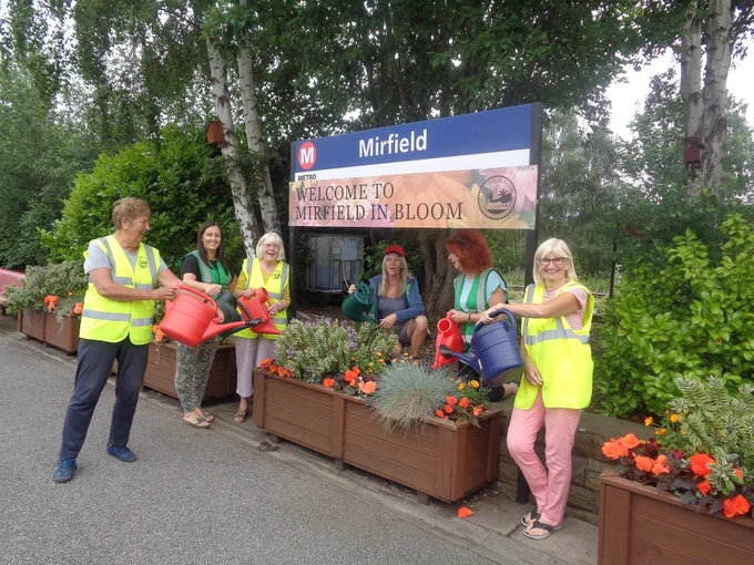 A group of volunteers stood around planters with watering cans. 