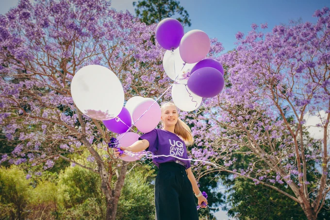 Girl holding purple balloons with flowering jacaranda behind her