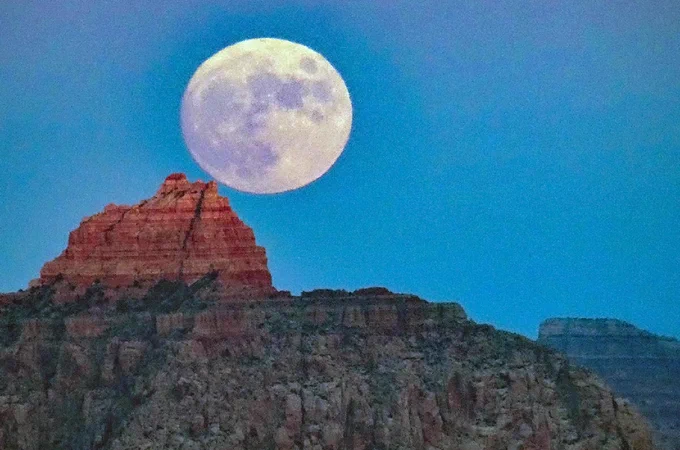 A brilliant full moon rising above a triangular shaped peak that is illuminated by the last rays of sunlight. NPS/M. Quinn

