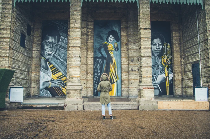 A person looks at murals of Una Marson, Evelyn Dove and Winifred Atwell by Carleen De Sozer.