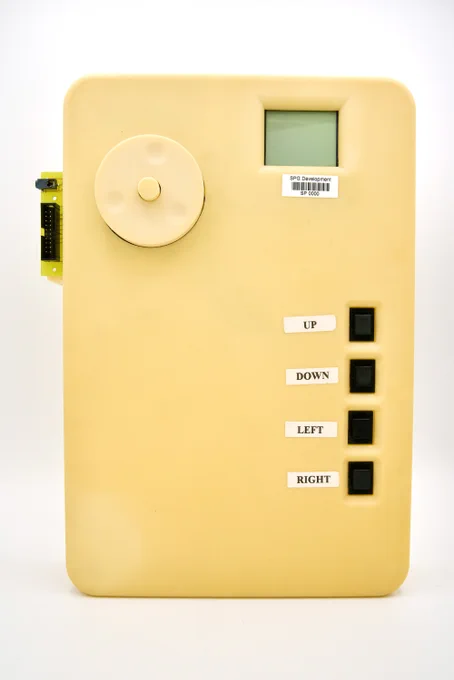 A photograph of a prototype original iPod. The case is extremely large and has yellowed over time. There is a funky clickwheel, the final size LCD screen, and large black buttons labelled UP, DOWN, LEFT and RIGHT.