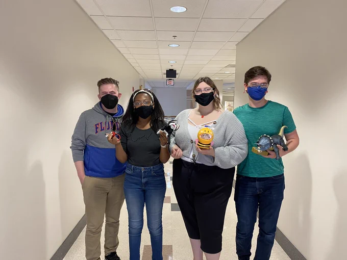 Four former high school robotics team members hold adapted toys.