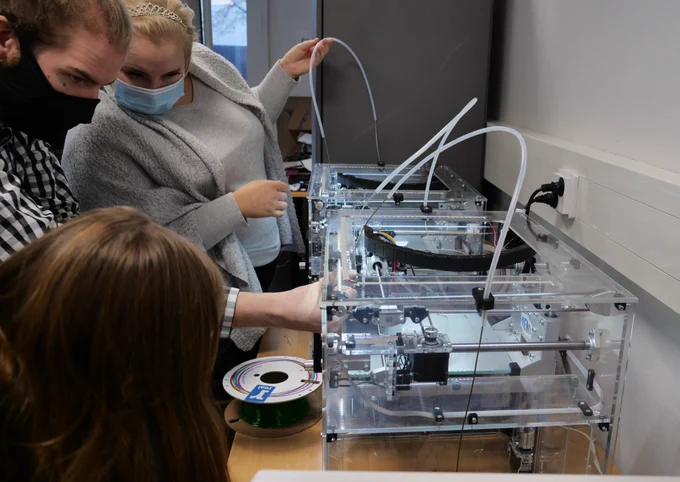 3D-tulostimen ympärillä 3 ihmistä kokeilemassa tulostamista