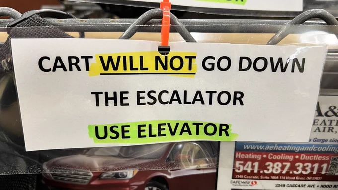 A sign that says “Cart will not go down the escalator. Use elevator.” There is a yellow and green highlighter.