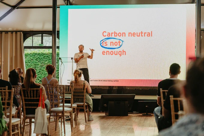 Christian Kroll, founder of Ecosia, speaking at DevBreak with a presentation slide at the back saying "Carbon neutral is not enough". 