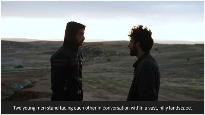 Two young men stand facing each other in conversation within a vast, hilly landscape.