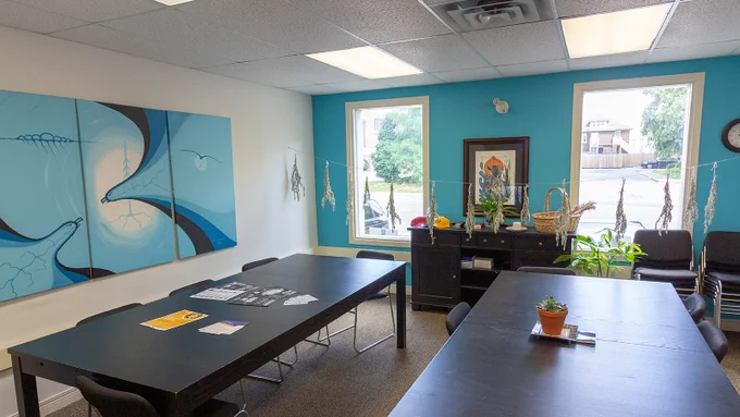 An indoor view of a gathering space in the Indigenous Student Centre on Laurier's Brantford Campus. The room is bright, with plants hanging from the ceiling and work by Indigenous artists on the walls.