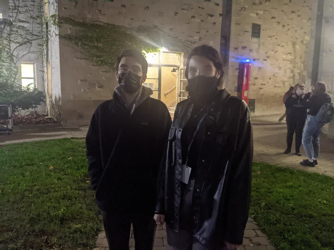 Two people in coats and masks outdoors in the evening 