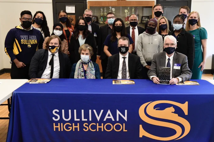A group of Sullivan High School students, legislators, and university of Illinois administrators pose for a photo inside a high school. 