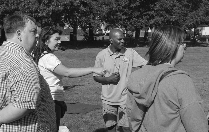 A black and white photo of four people, two men and two women, pointing to something out of shot in a park in Coventry.