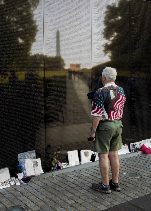 A veteran pays tribute to fallen military members at the black marble Vietnam Veterans Memorial. A reflection of the Washington Monument appears on the shiny surface of the memorial