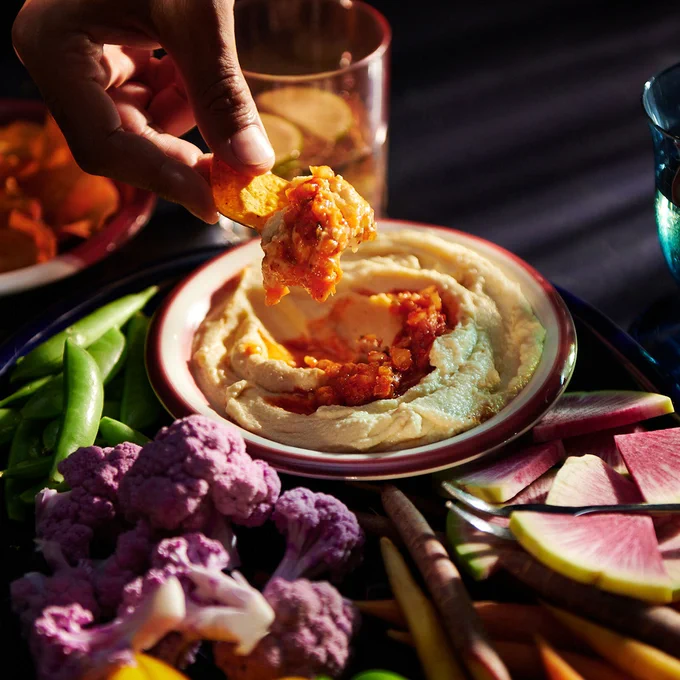 a hand dipping a chip into a bowl of kimchi hummus 