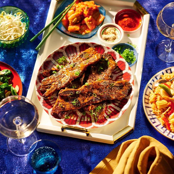 a dinner table set with lots of toppings and side dishes. the main dish is a plate of kale beef ribs