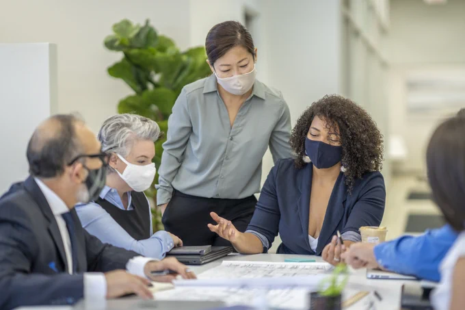 Group of business people sitting at boardroom table wearing masks.