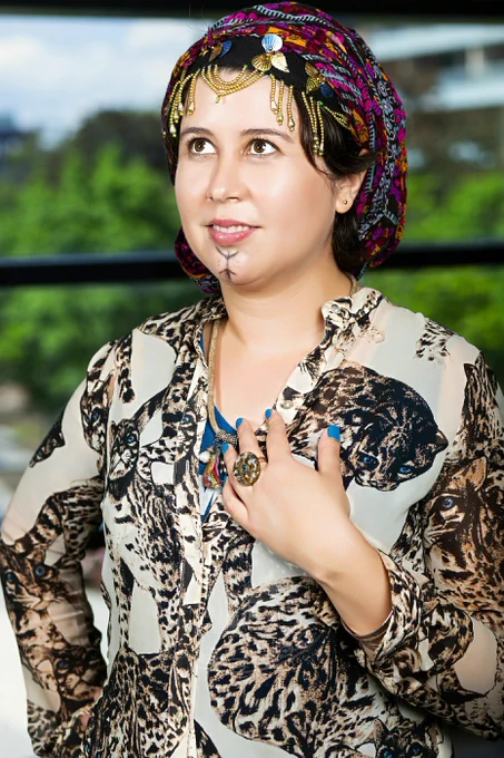 Photo of artist wearing a leopard print top, an Amazigh (Berber) headdress and a beautiful smile on their face.