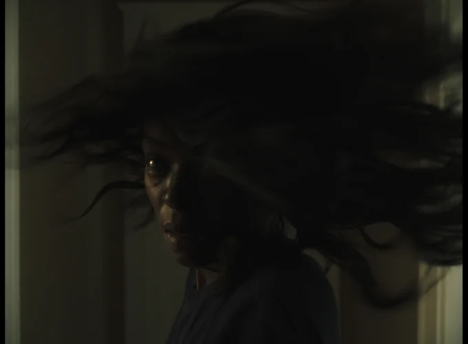 Image description: A photo of a dark-skinned woman turning towards the camera. Her long, straight hair is whipping around her head.