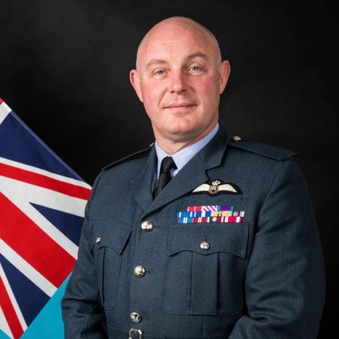A professional photo of AVM Smyth dressed in his RAF uniform with a Union Jack flag in the background.