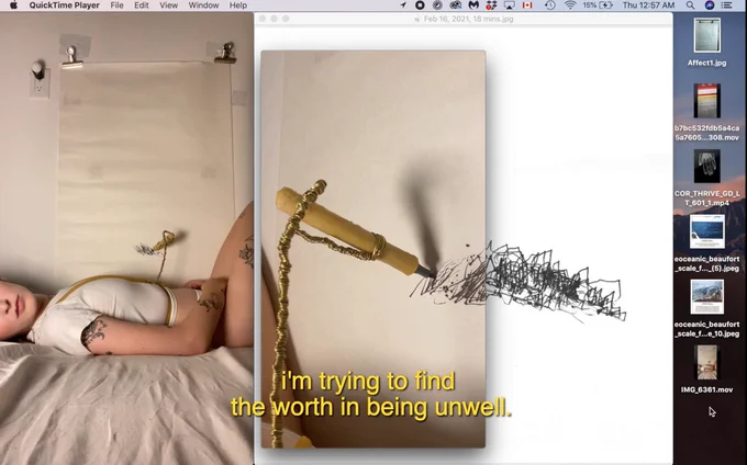 A Screenshot of Hannah’s computer desktop. Yellow text at the bottom reads: ‘I’m trying to find the worth in being unwell’ On the far left there is an image go Hannah lying in bed, wearing a latex and brass harness that holds a marker above her stomach. Mounted to the wall on her left, there is a large piece of paper which has some some scratch-like black lines from the marker. To the right of that image, there is a close up of the marker making its marks on the paper. The close-up of the marker overlaps a scan of the drawing.