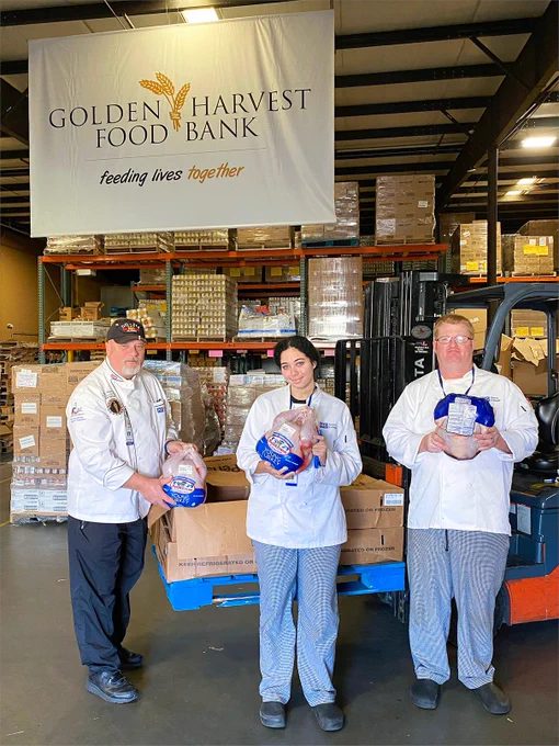 A chef and two students hold up ready-to-cook turkeys in front of the Golden Harvest Food Bank warehouse.