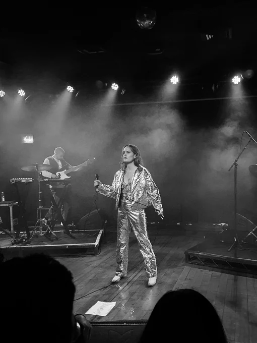 Kelly Zutrau lead singer of the band wet on stage in a shiny silver jacket and trousers and white cowboy boots